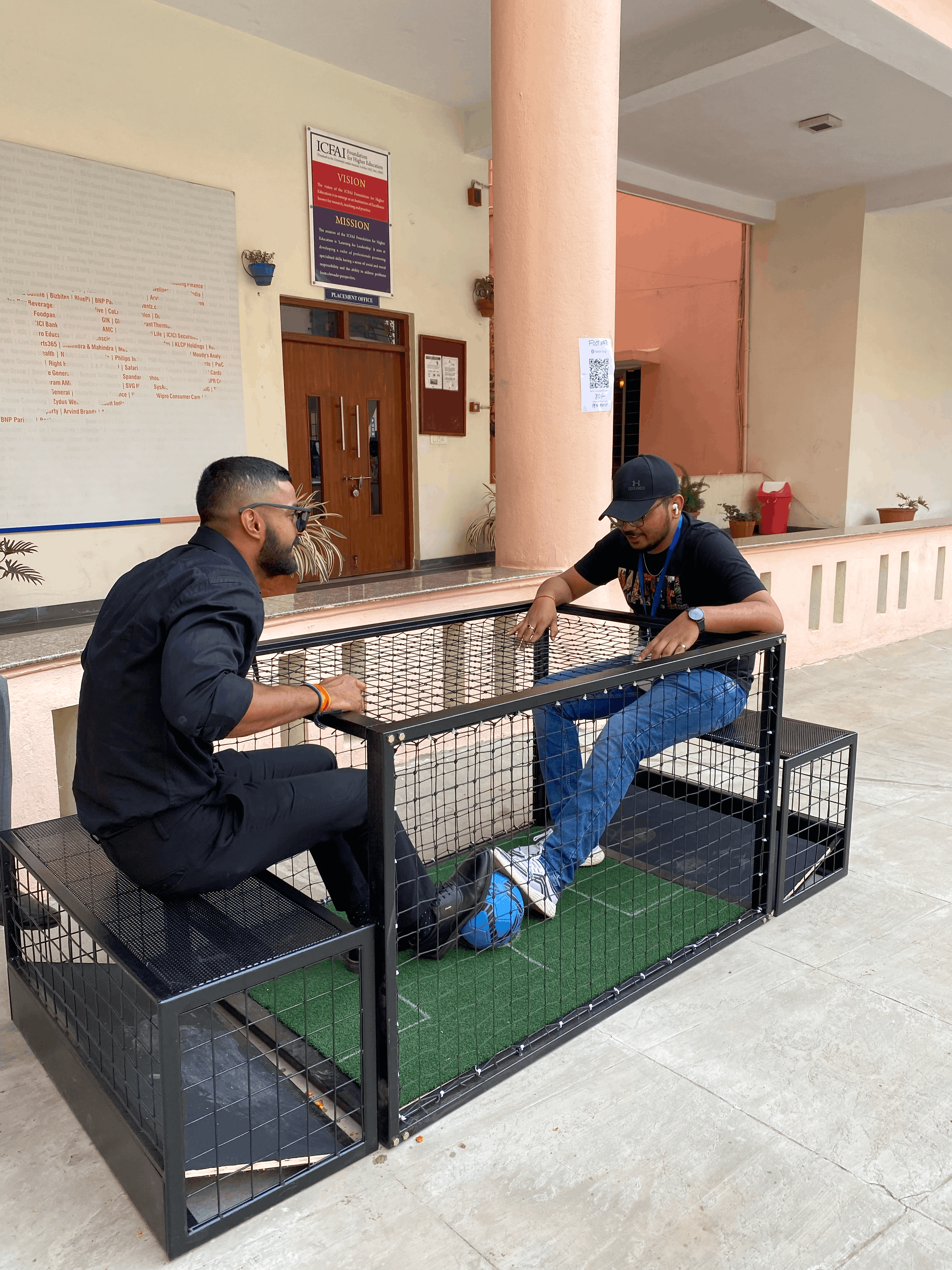 foot war table soccer game in action, two players seated kicking ball, enclosed arena with nets, LED scoreboard, arcade environment, dynamic lighting