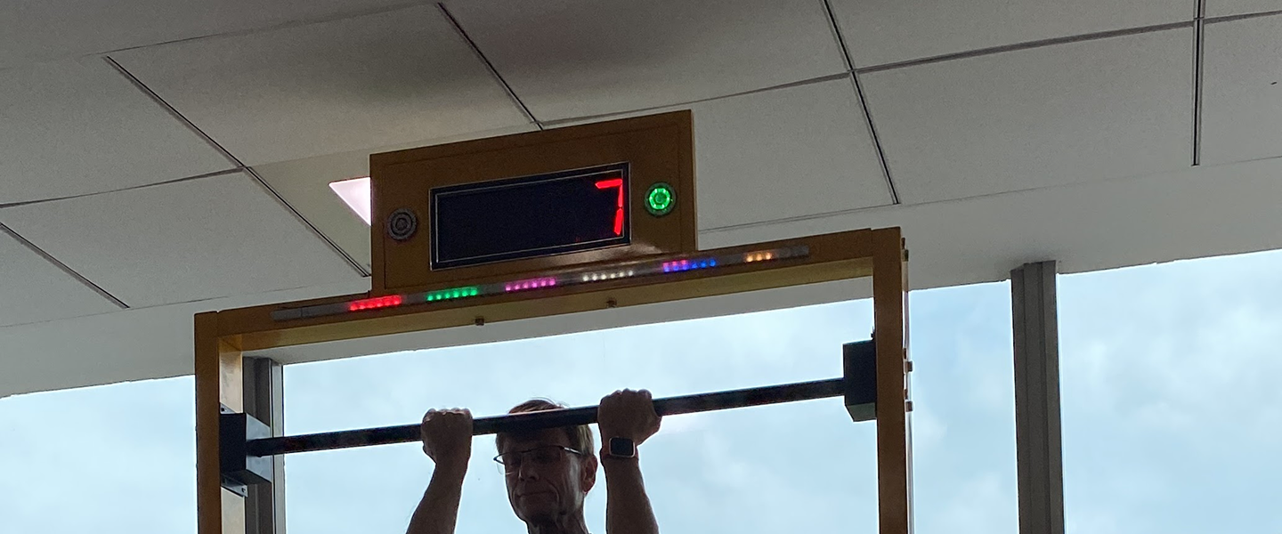 hang the bar challenge in action, player gripping rotating bar, digital countdown timer, crowd watching, competitive zone atmosphere, professional photography