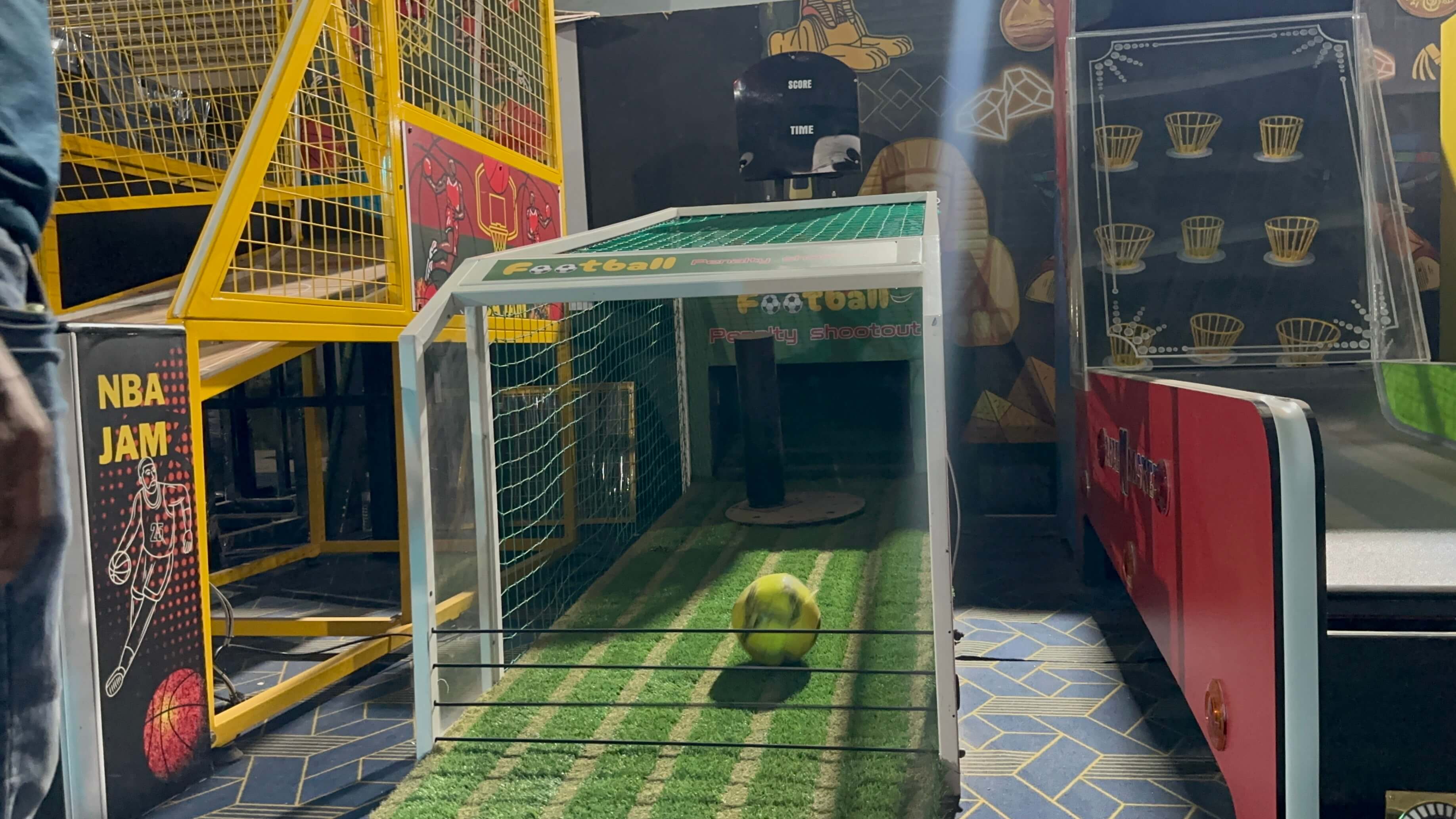 penalty shoot out soccer arcade game in action, player kicking ball at illuminated targets, LED scoreboard display, modern sports arcade interior, dynamic lighting
