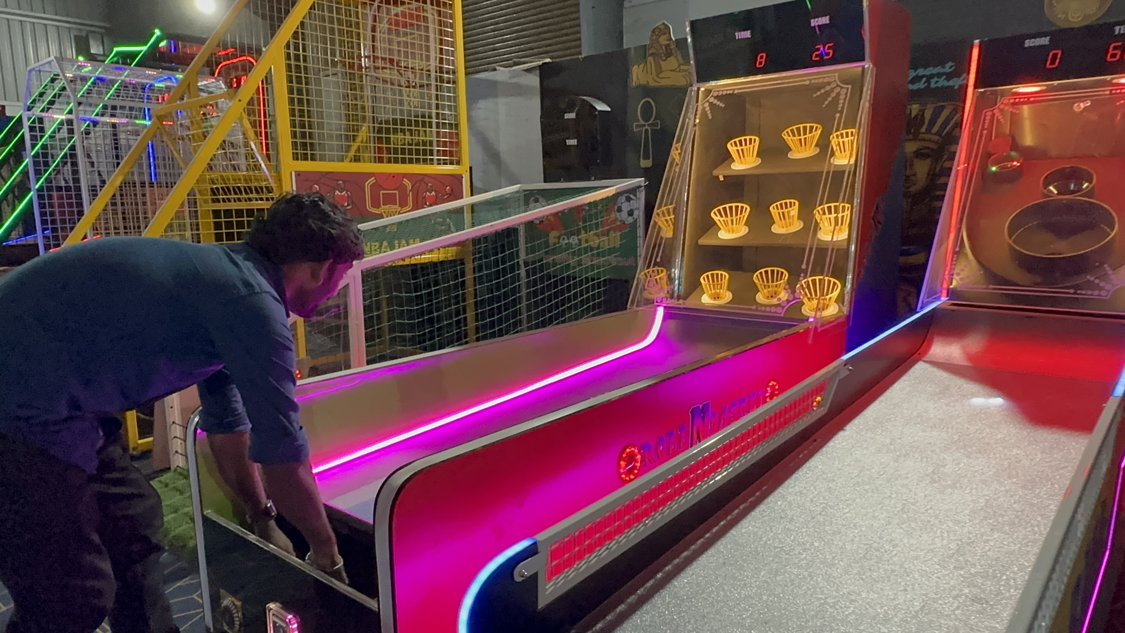 Rollen Basket arcade machine in action, player rolling ball up ramp, LED scoring baskets illuminated, modern arcade setting, dynamic lighting, professional photography